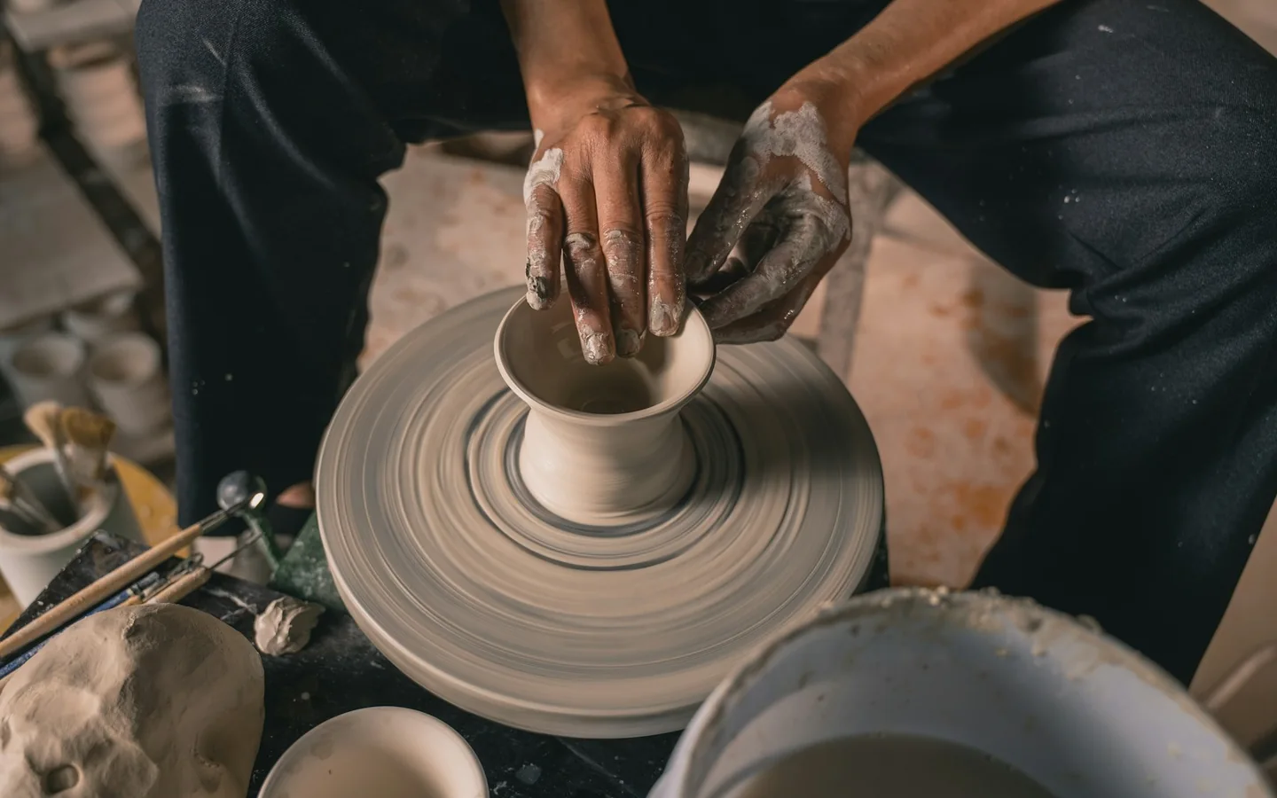 Hands shaping a clay vessel on a pottery wheel